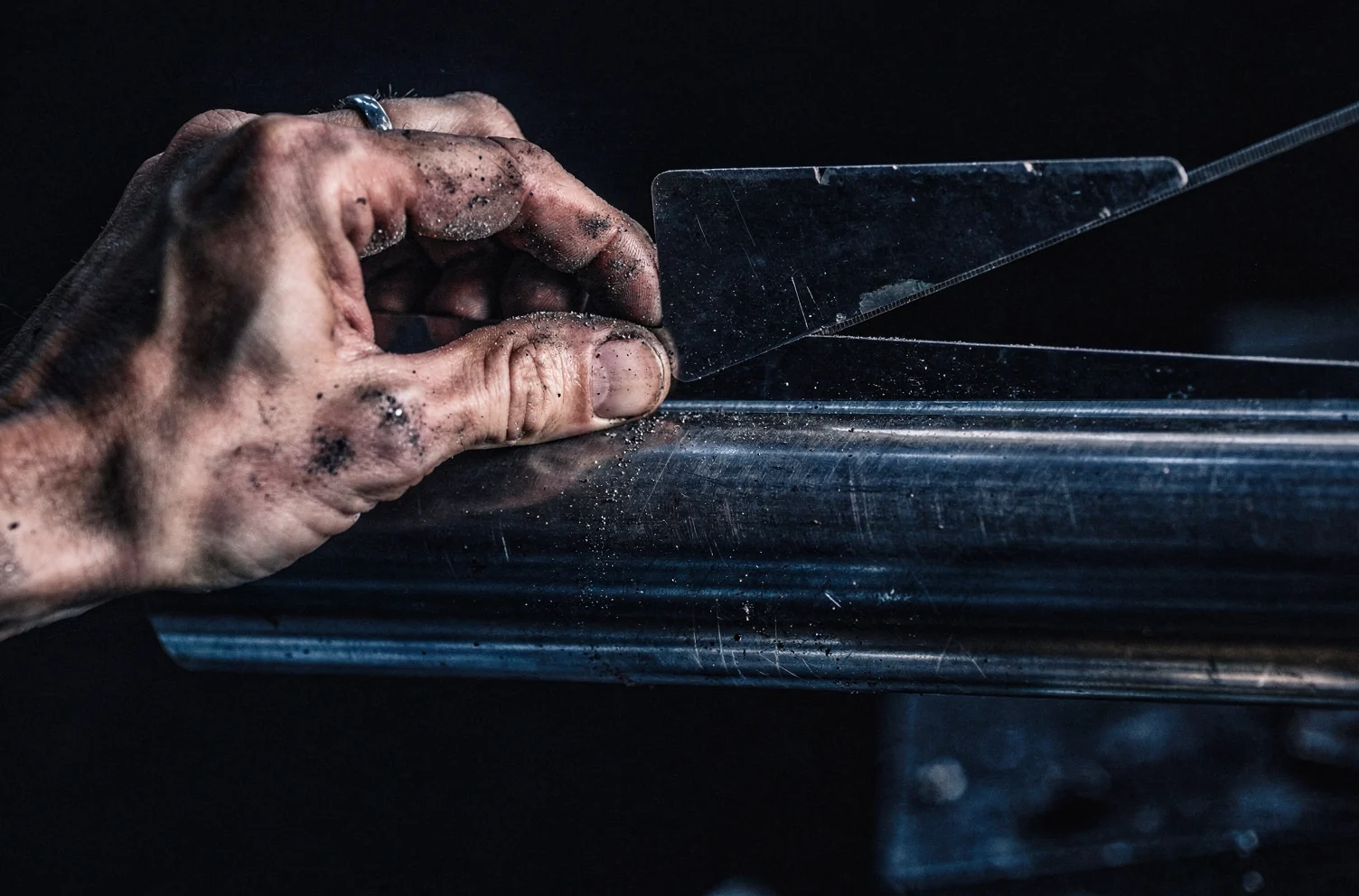 A hand sliding a thin steel feeler gauge blade into the gap between a straight edge and a machined steel shaft resting on a dark bench