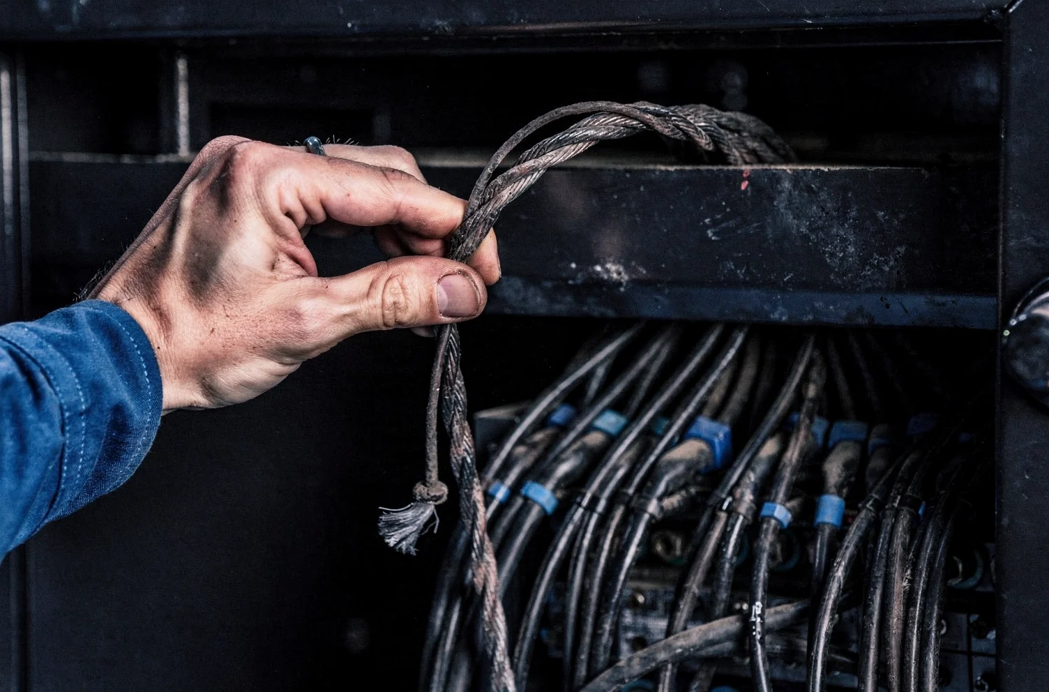 A hand pulling a single cable clear of a dense bundled loom of identical cables inside the open back of a dark equipment cabinet