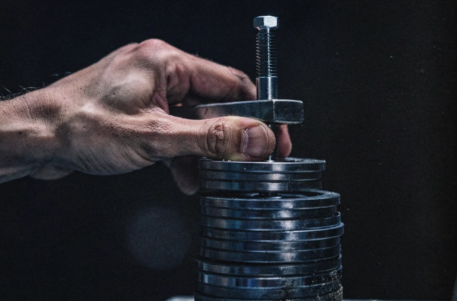 A hand sliding a thick steel washer onto a vertical threaded rod above a stack of identical washers.