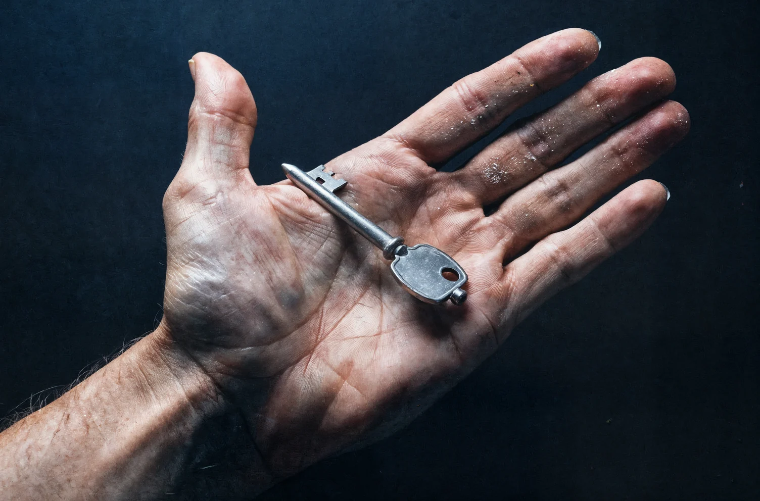 One open hand holding a single heavy plain steel key across the palm against a dark background